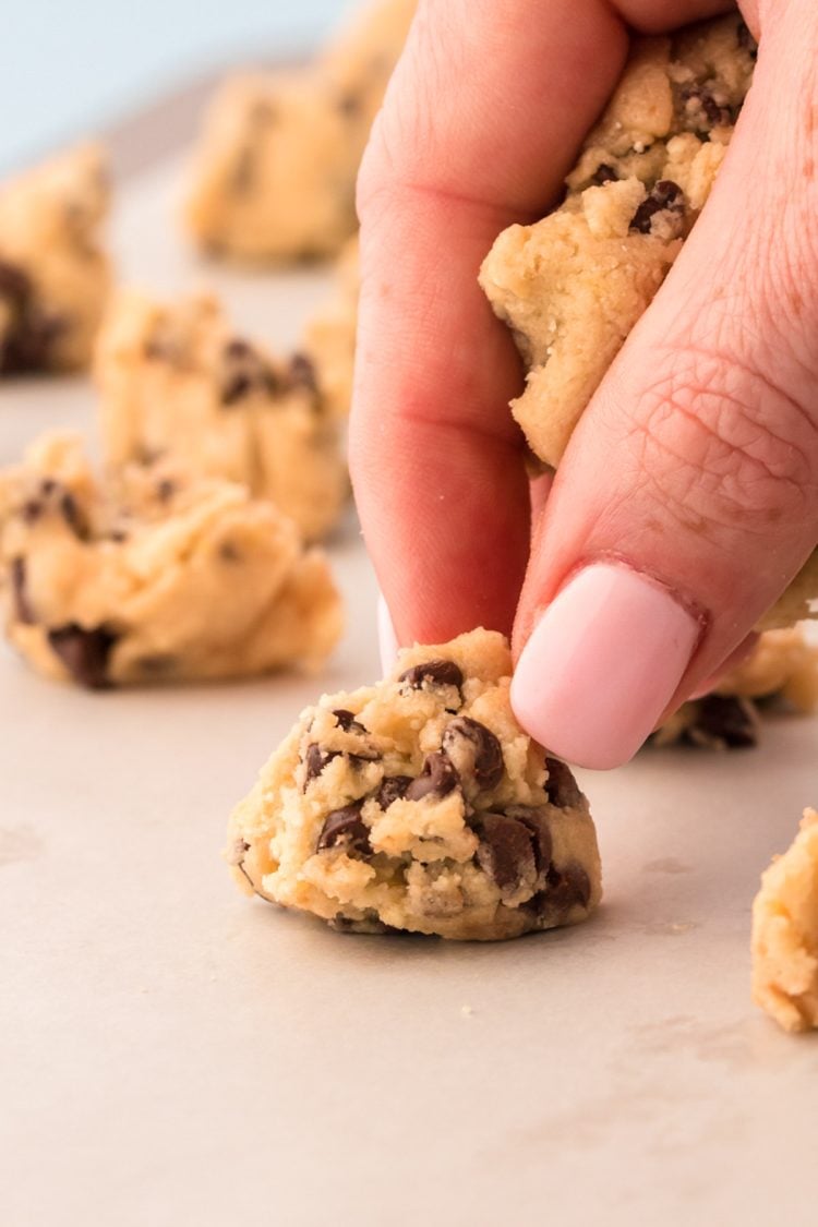 A woman's hand portioning out cookie dough on a parchment lined cookie sheet.