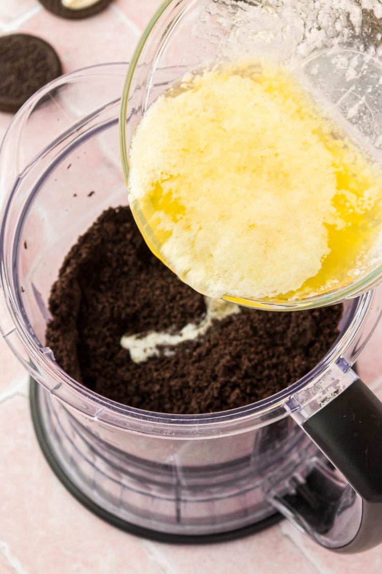 Melted butter being poured into a food processor with Oreo crumbs.