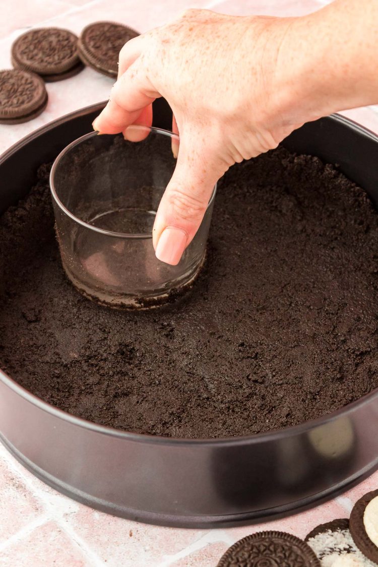 An Oreo crust being pressed into a springform pan.