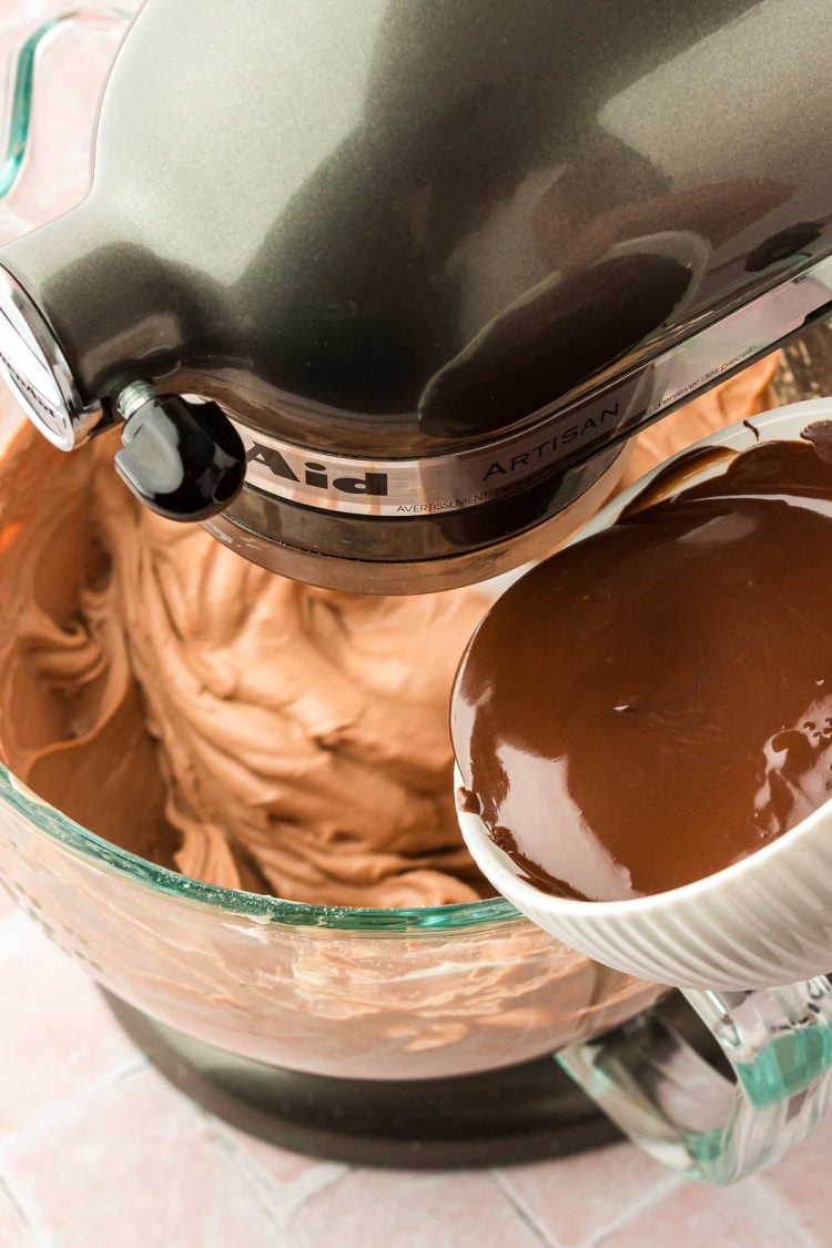Melted chocolate being poured into a mixing bowl with chocolate cheesecake filling in it.
