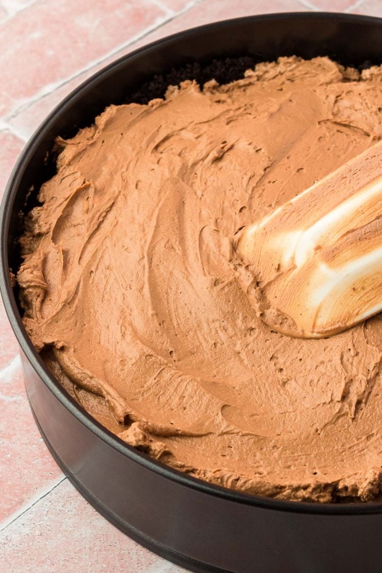 Chocolate cheesecake filling being smoothed out in an oreo crust in a pan.