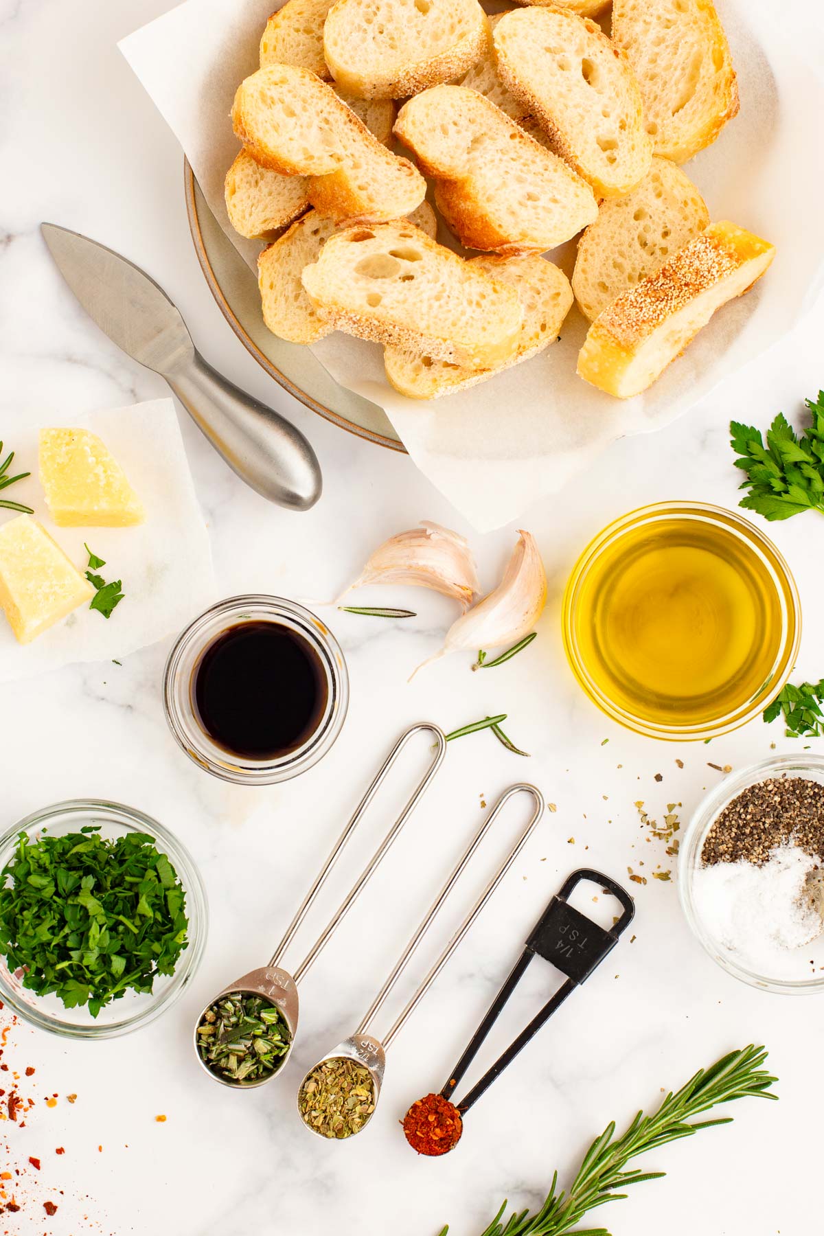 Overhead photo of ingredients to make olive oil bread dip on a white table.