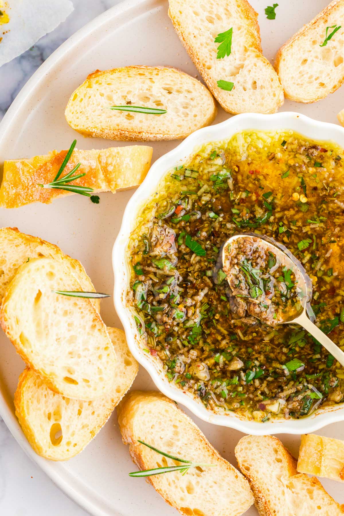 Overhead photo of slices baguette on a white plate with a dish of dipping oil and herbs.