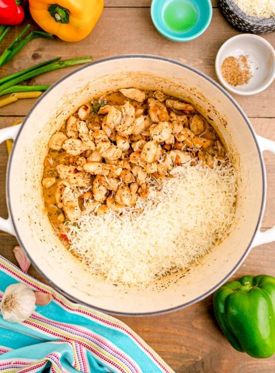 Chicken and parmesan cheese being added to a pot with peppers and broth.