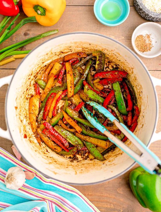 Sliced bell peppers being cookies in jerk seasoning in a Dutch oven.