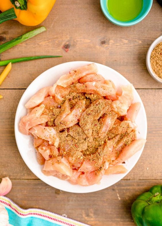Chicken being seasoning on a white plate.