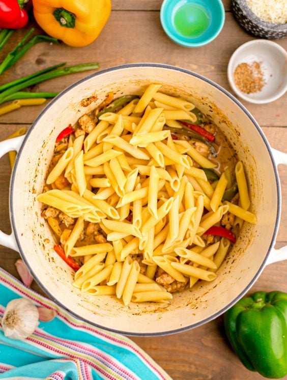Pasta added to a pot with chicken and peppers and sauce to make rasta pasta.