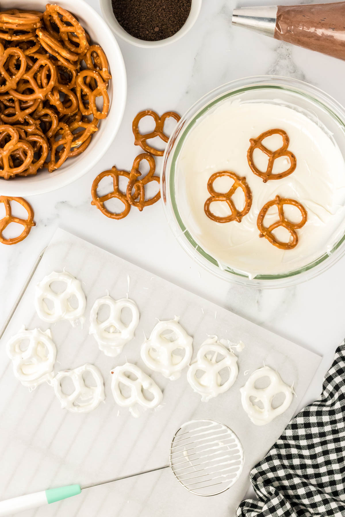 Overhead photo of pretzels being dipped in white chocolate and placed on parchment.