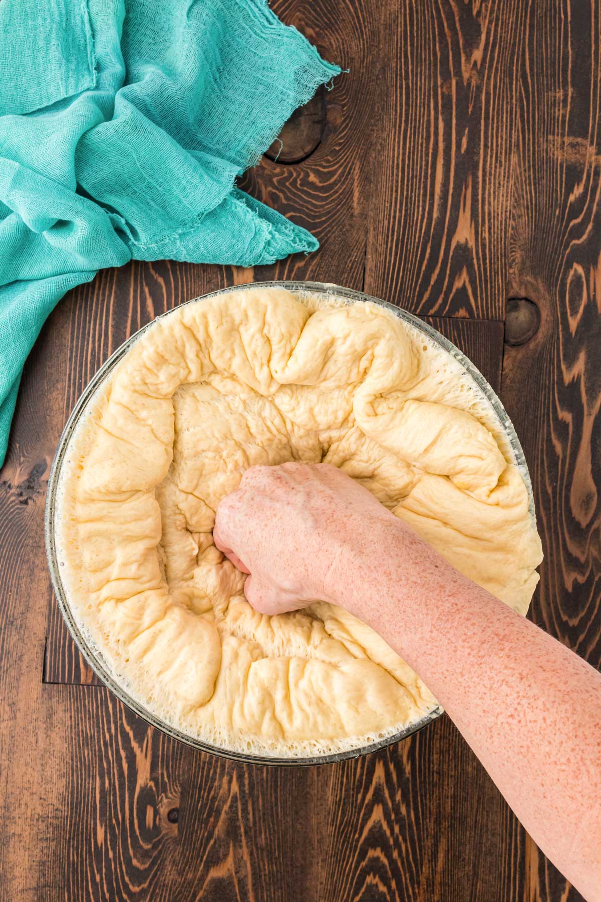 A woman's hand punch into a bowl of dough.