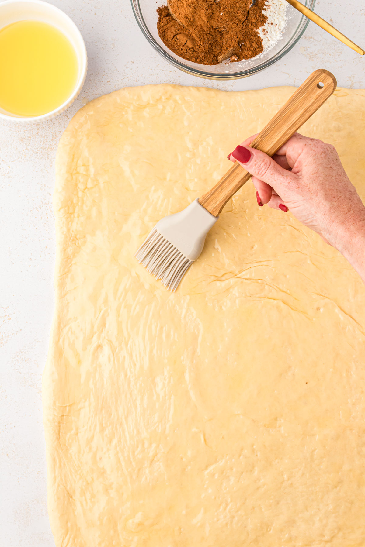 A pastry brush brushing dough with butter to make sweet rolls.