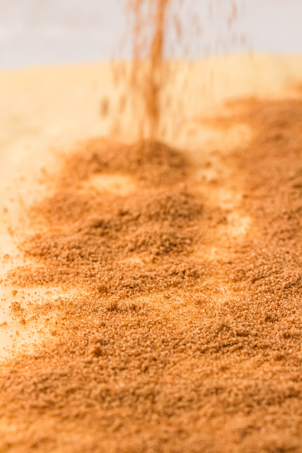 Cinnamon sugar being sprinkled on top of a buttered rectangle of dough.