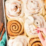 Overhead photo of a pan of freshly baked cinnamon rolls being covered by icing.