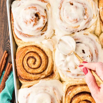 Overhead photo of a pan of freshly baked cinnamon rolls being covered by icing.