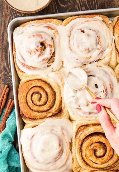 Overhead photo of a pan of freshly baked cinnamon rolls being covered by icing.