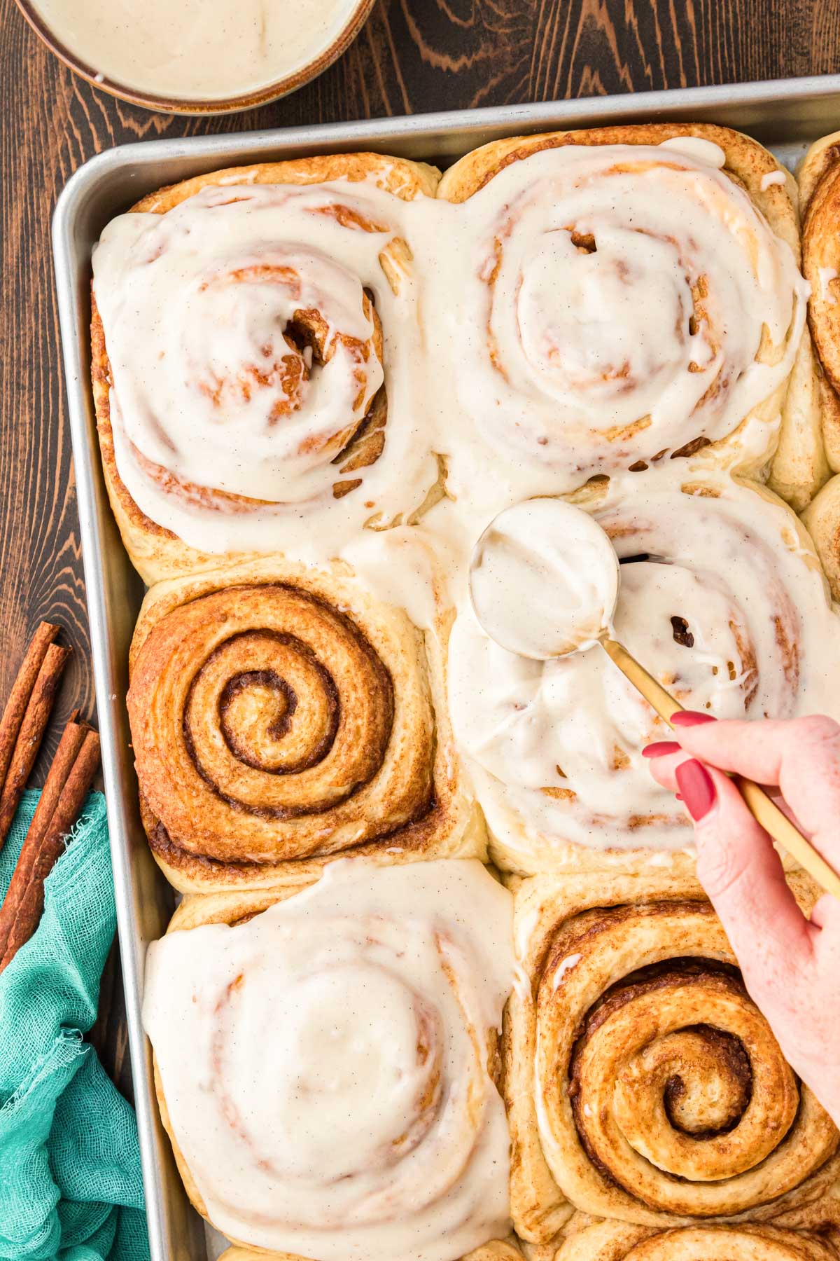 Overhead photo of a pan of freshly baked cinnamon rolls being covered by icing.
