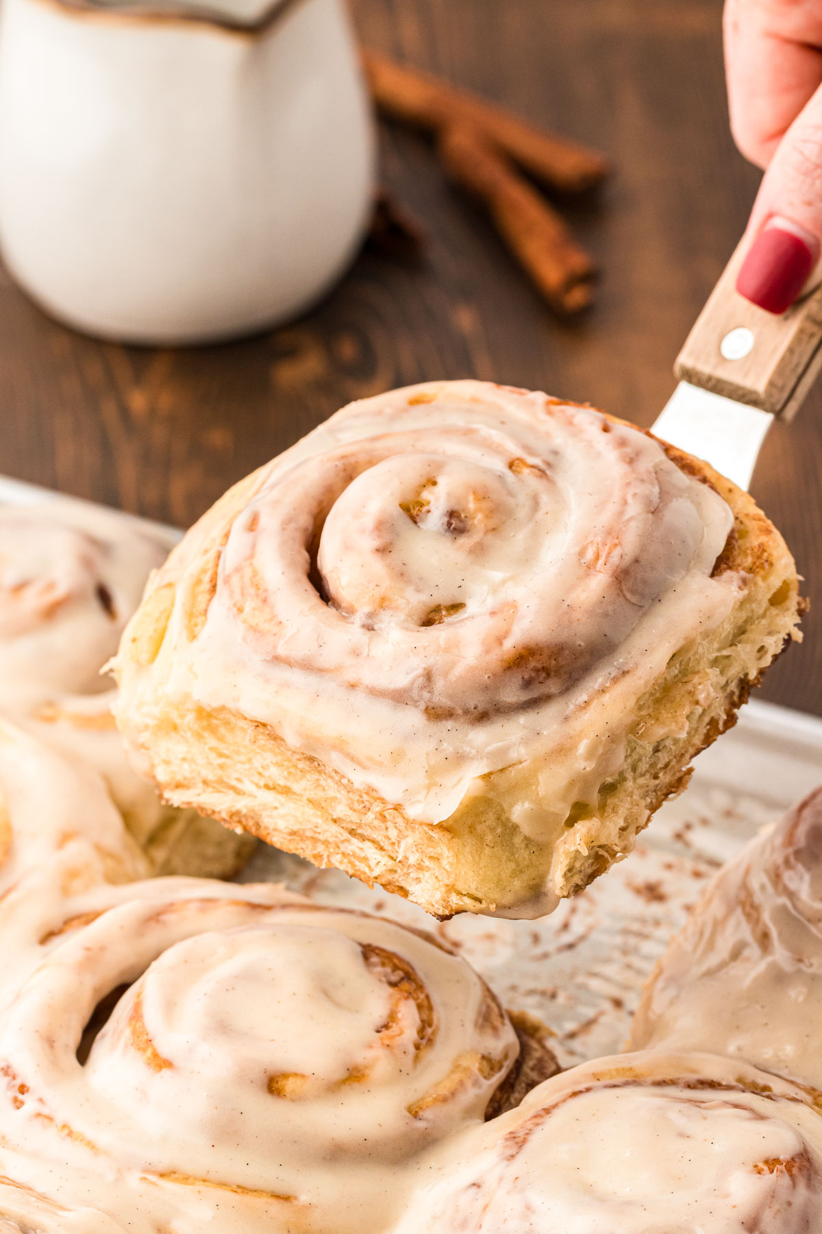 A spatula lifting a cinnamon roll away from the baking pan.