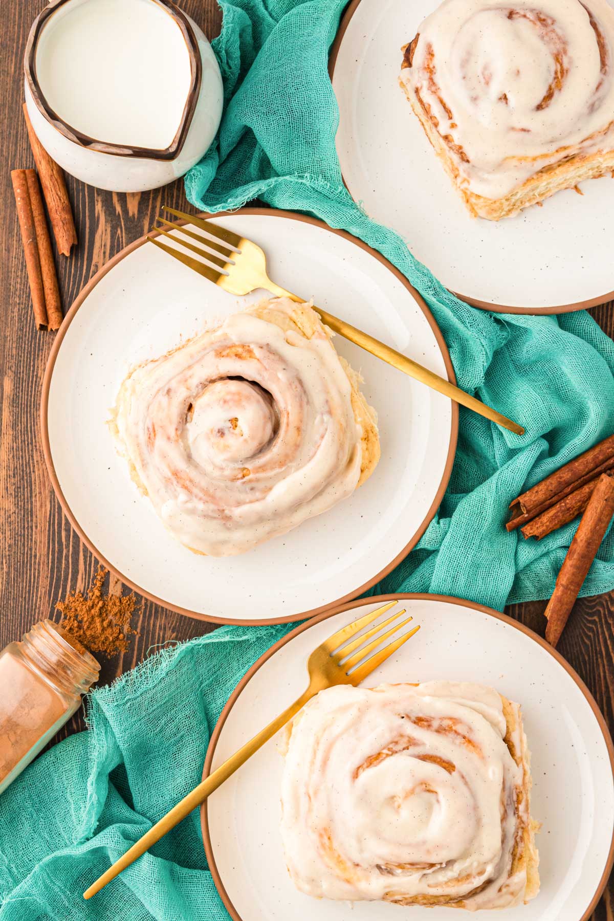 Overhead photo of cinnamon rolls on a plate on a wooden table with a teal napkin.