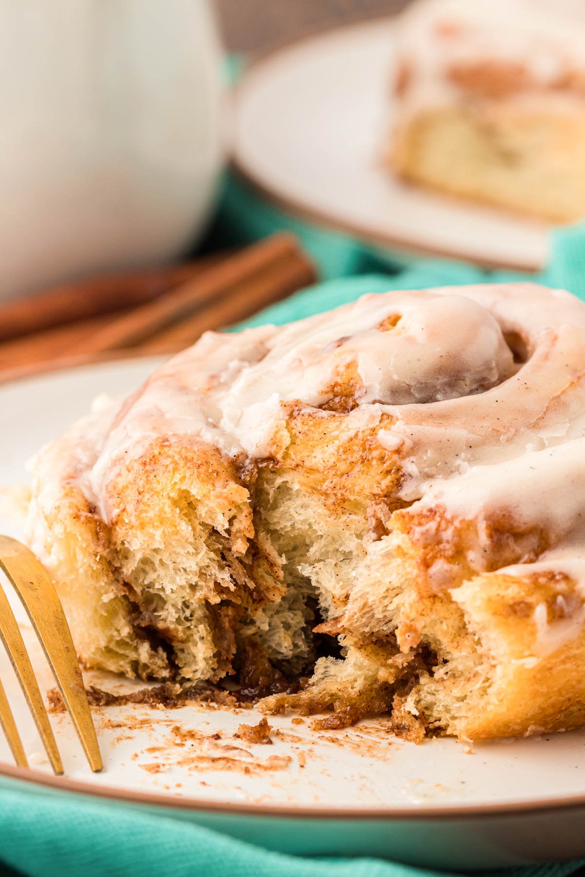 A soft cinnamon roll on a white plate with a bite missing out of it.