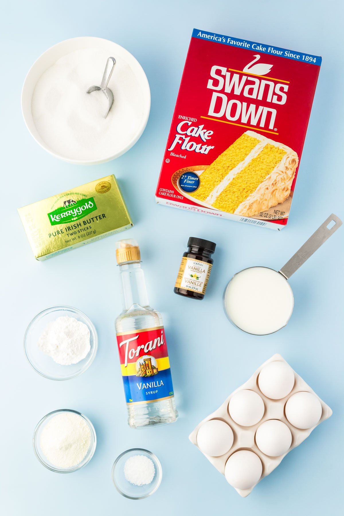 Overhead photo of ingredients used to make vanilla white cake on a blue surface.