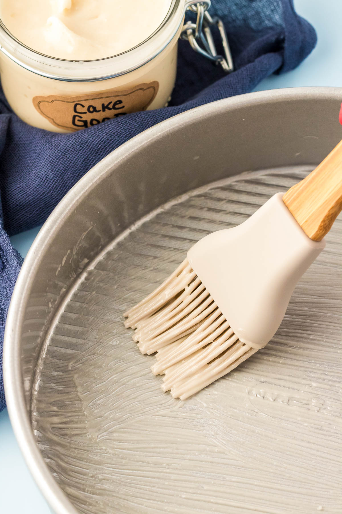 Cake goop being brushed onto a round cake pan.