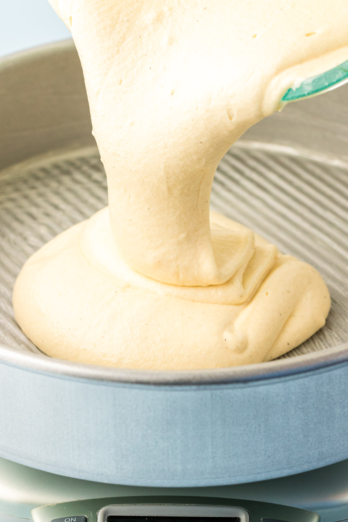 White cake batter being poured into a cake pan.