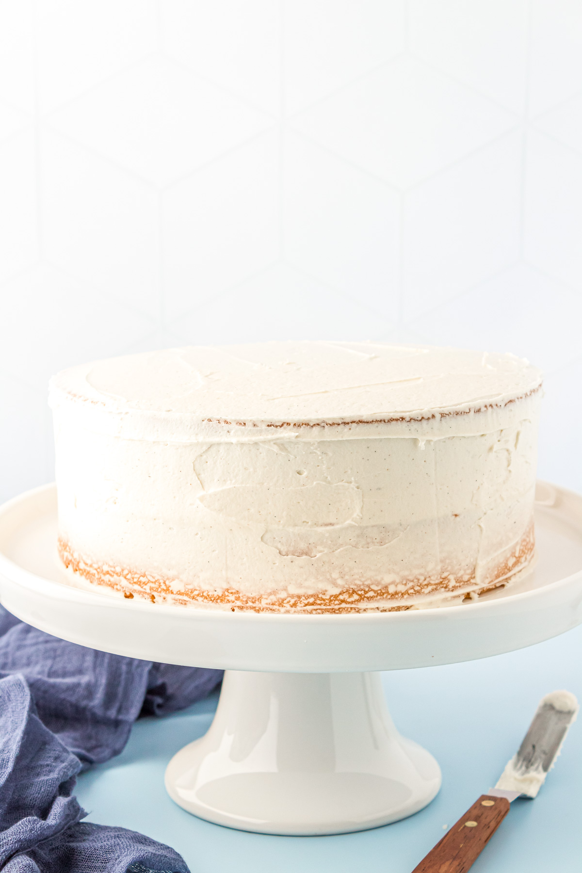 A vanilla cake with a vanilla frosting crumb coat on a white cake stand.