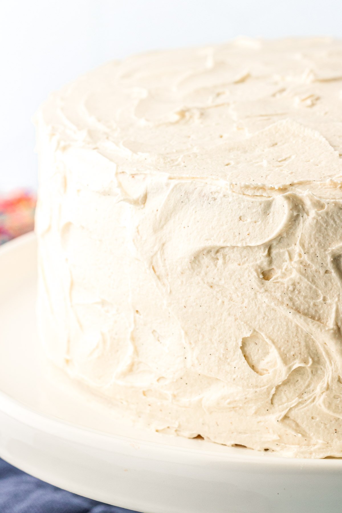 Vanilla frosted cake on a white cake stand.