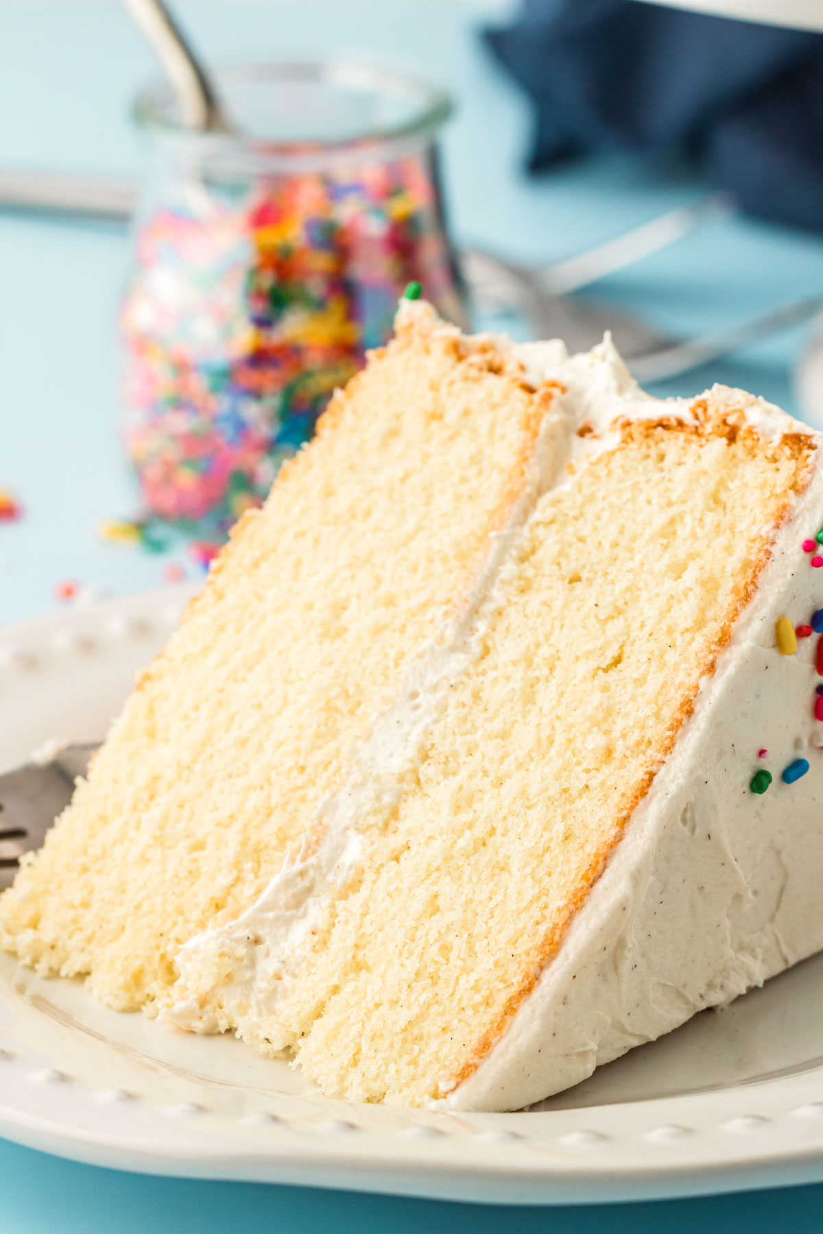 A slice of white vanilla cake on a white plate.