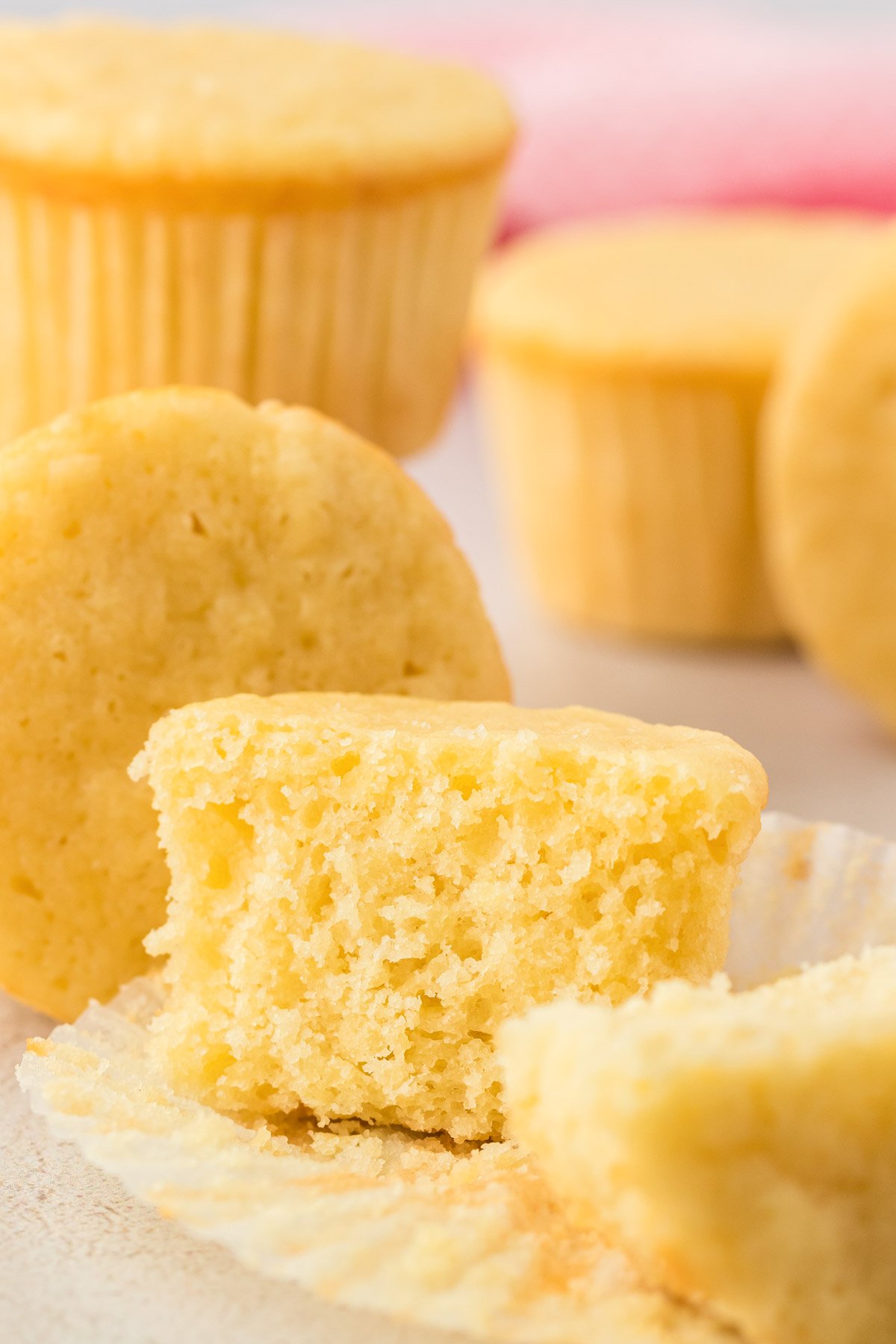 A plain yellow cupcake cut in half to reveal texture. Other cupcakes in the background.