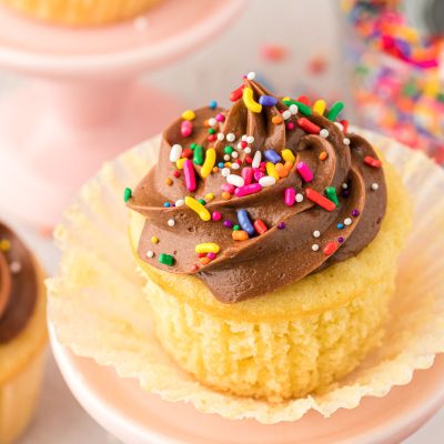 Yellow cupcake with chocolate frosting on a small cake stand with the wrapper pulled down to show texture.