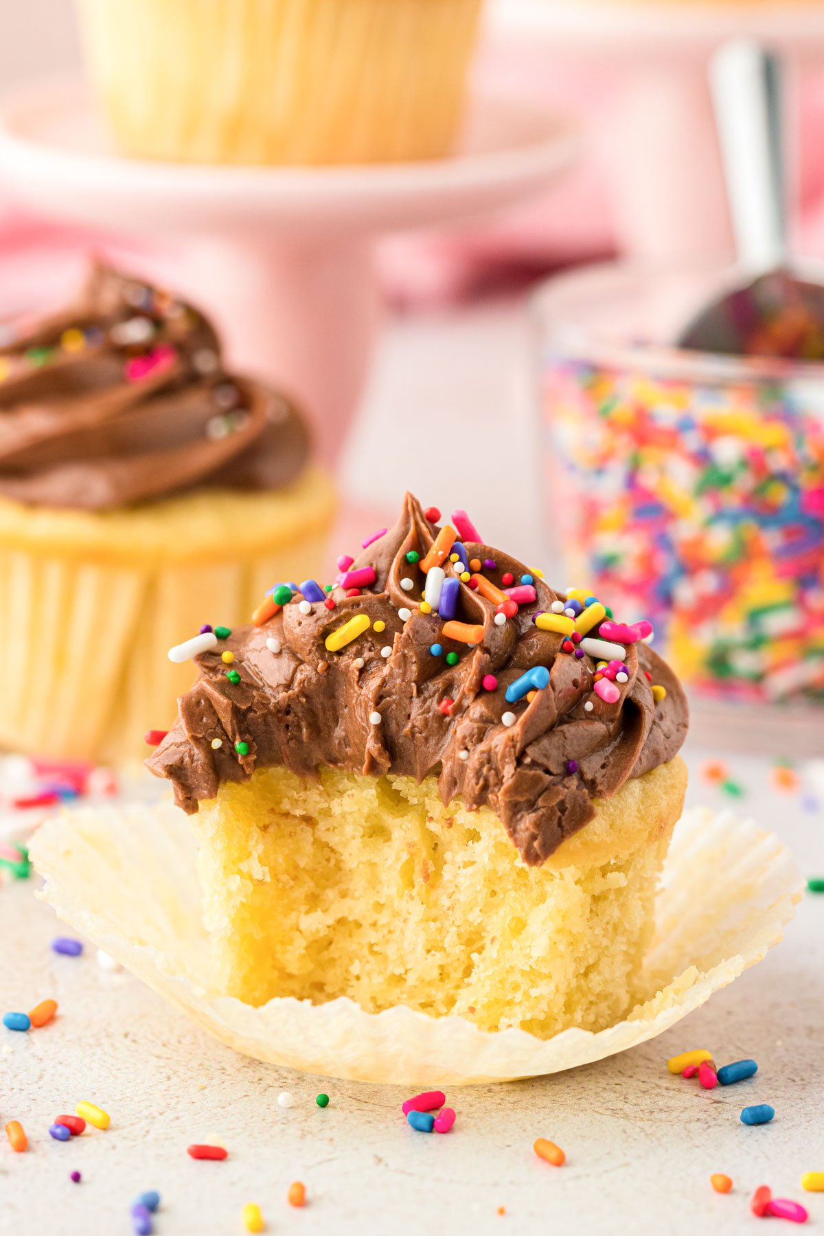 Yellow cupcakes with chocolate frosting, one is missing a bite.