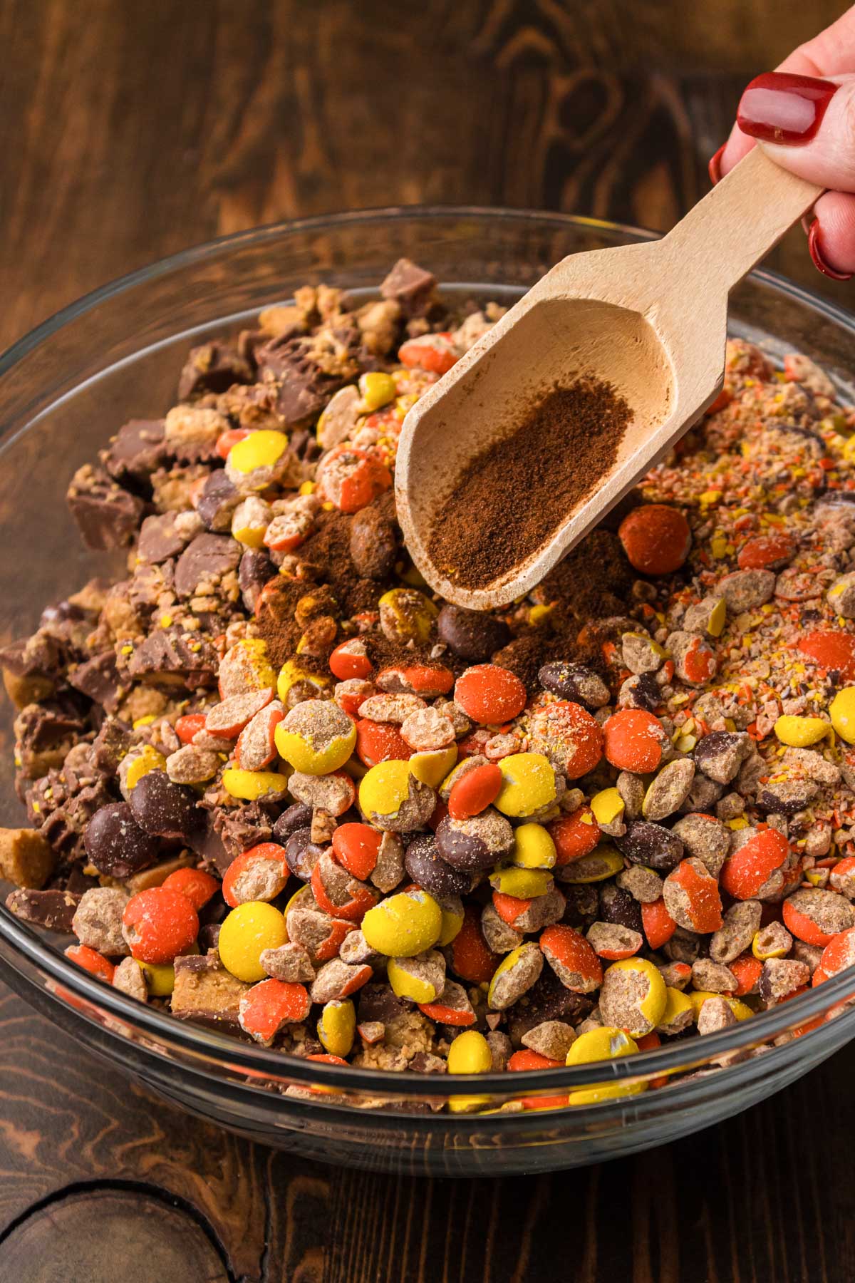 Ground espresso being added to a bowl of reese's pieces and chopped peanut butter cups.