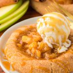 Apple pie cookie on a plate with a scoop of vanilla ice cream on top.