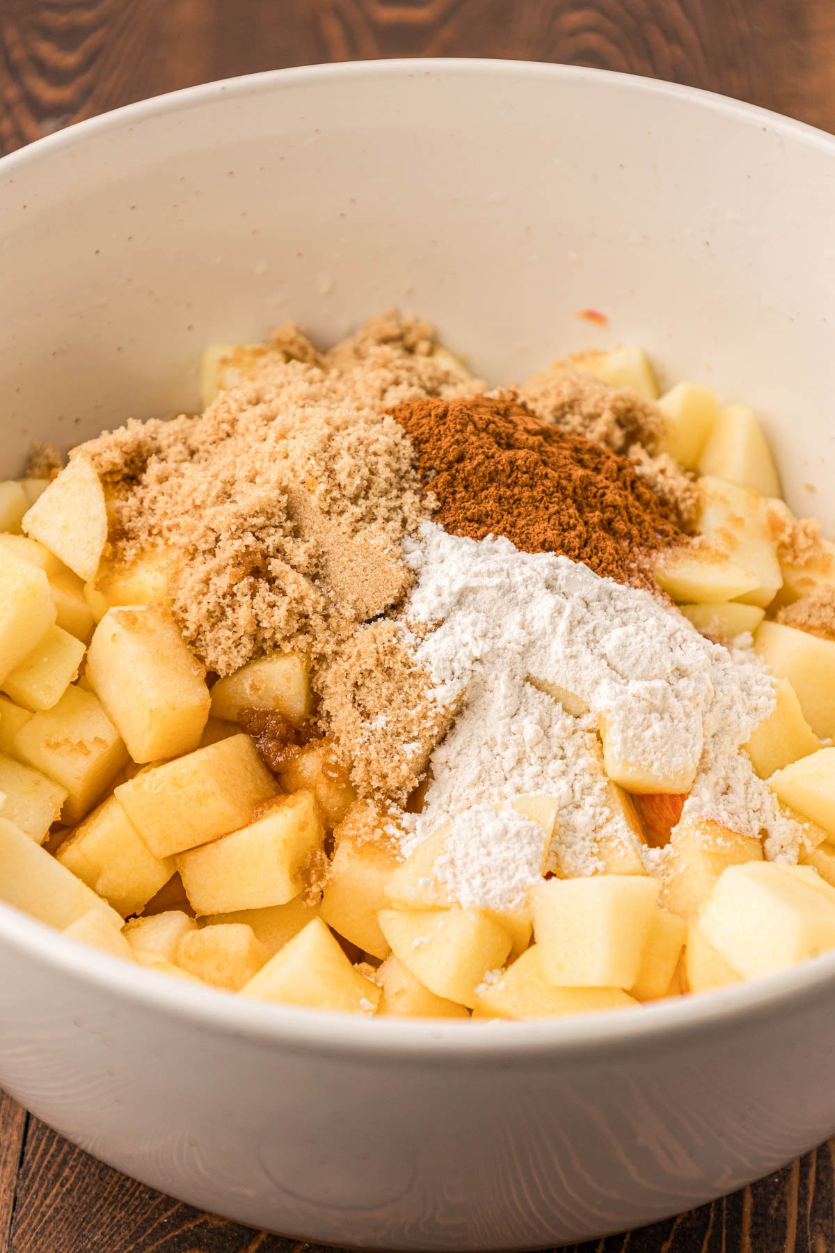 Chopped apples in a white bowl with flour and spices.
