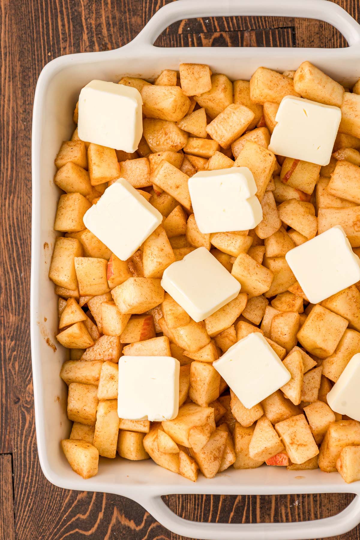 Overhead photo of apple crisp base in a baking dish with butter on top.