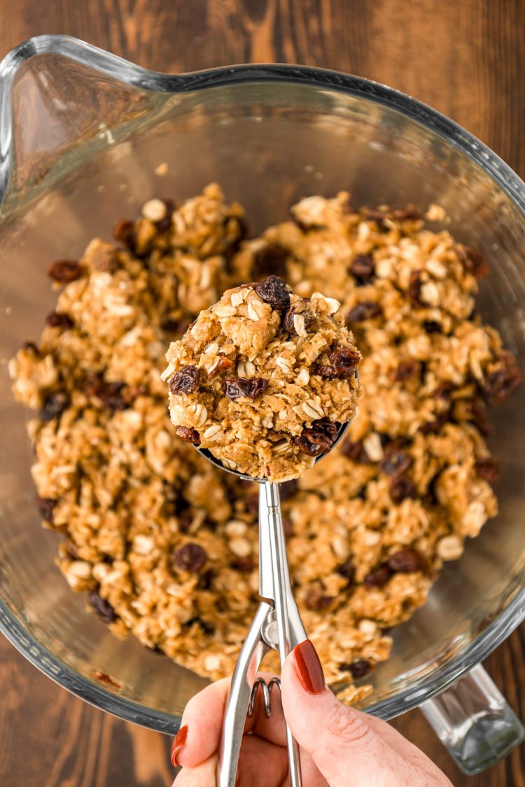 Oatmeal raisin cookie dough being scooped from a mixing bowl.