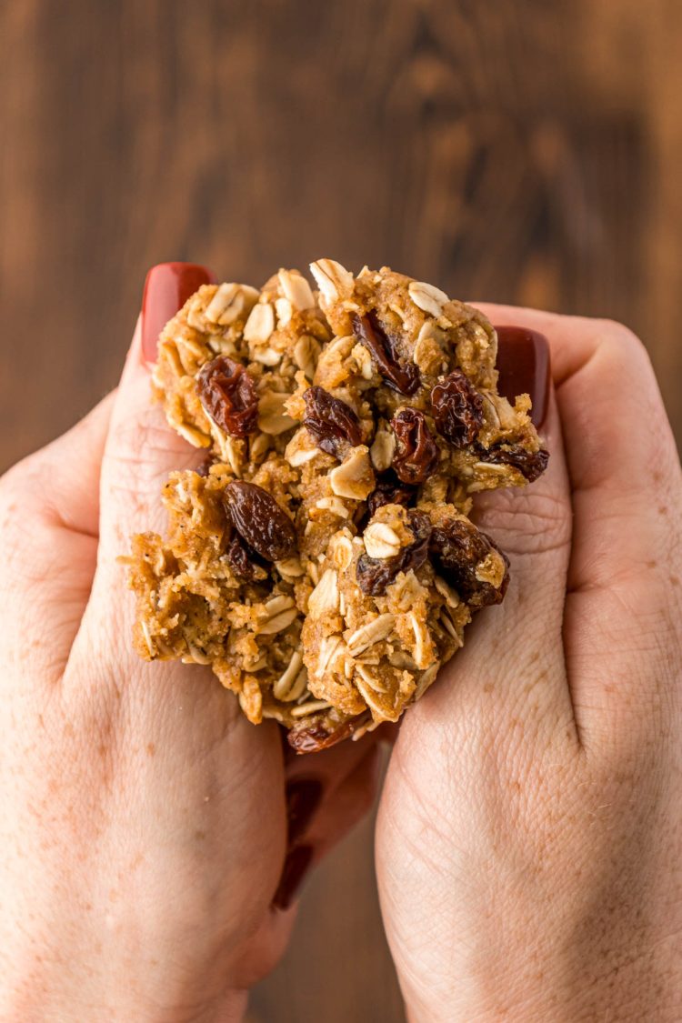 A woman's hand breaking a ball of oatmeal cookie dough in half.