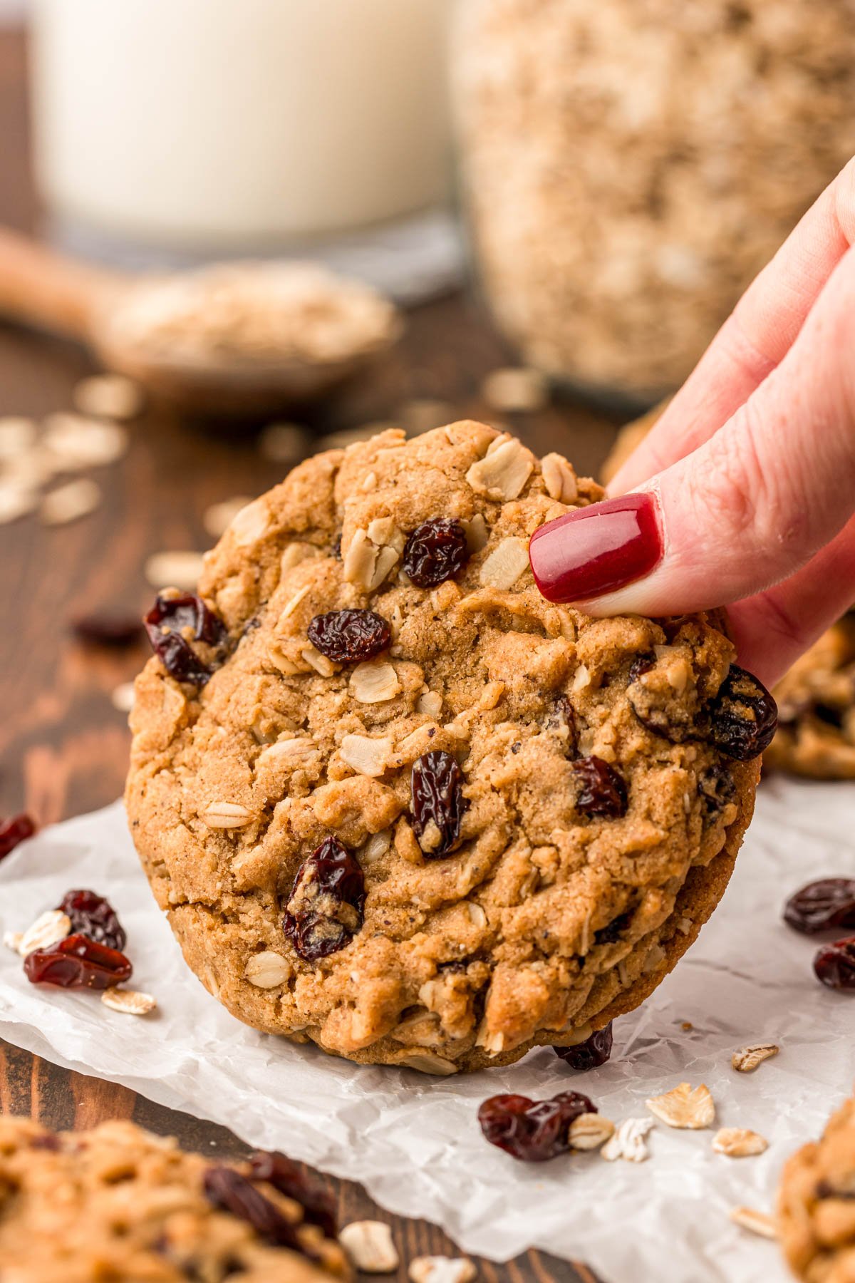 A woman's hand holding an oatmeal raisin cookie up off the table.