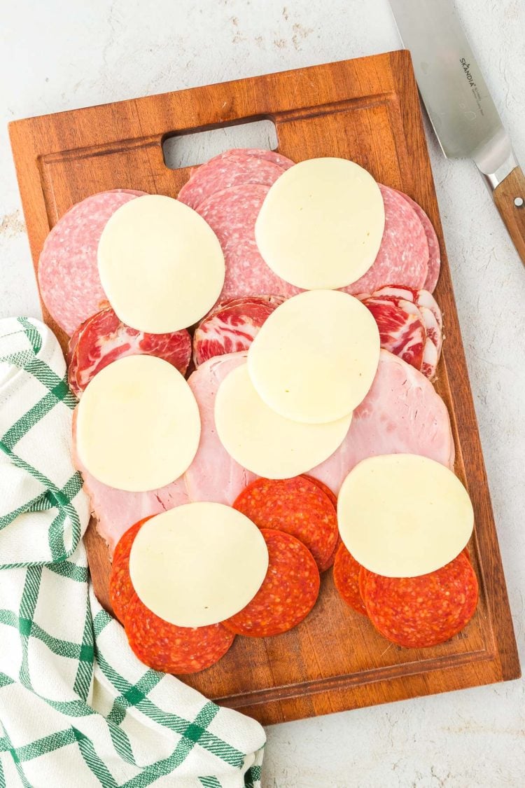 Layers of deli meat and cheese on a wooden cutting board.