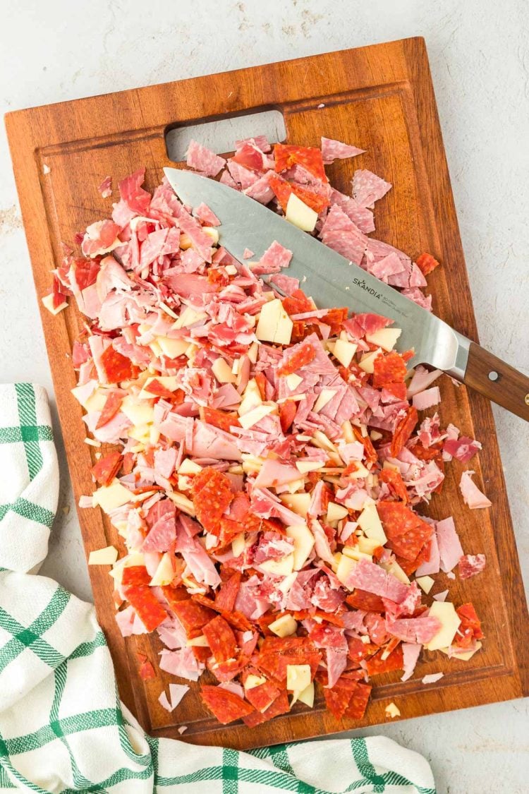 Deli meats and cheese chopped up on a wooden cutting board.