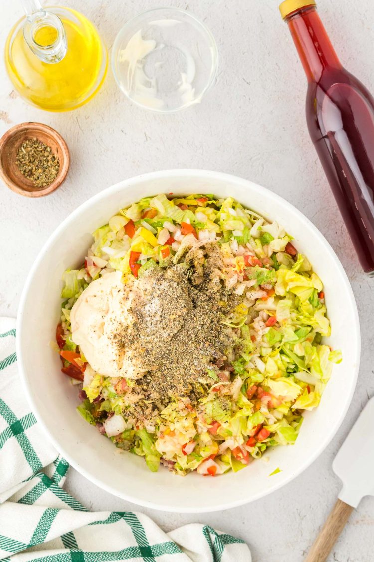 Seasoning, mayo, and oil being added to a bowl with chopped veggies and meat.