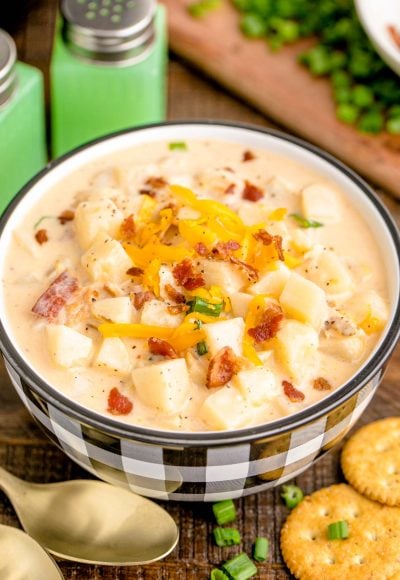 A close up photo of a white and black checkered bowl filled with potato soup on a wooden table.