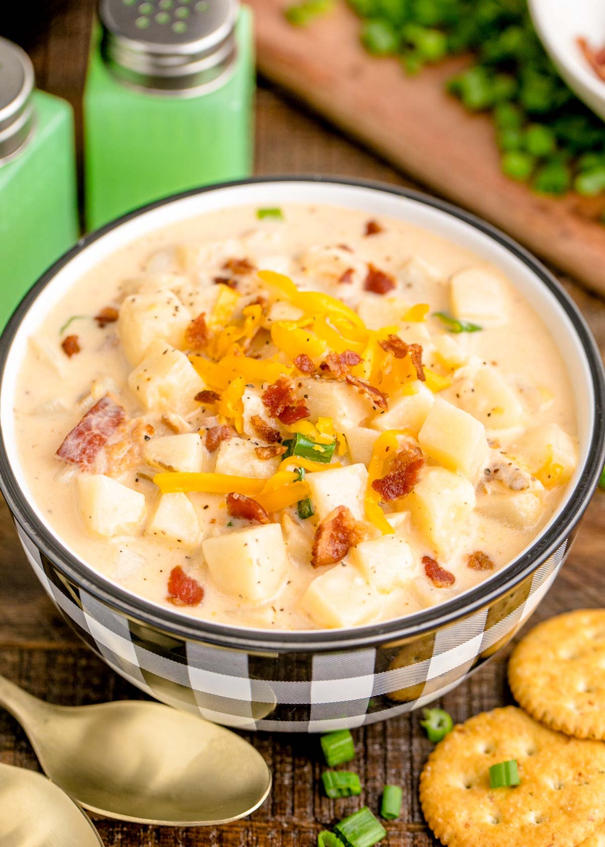 A close up photo of a white and black checkered bowl filled with potato soup on a wooden table.