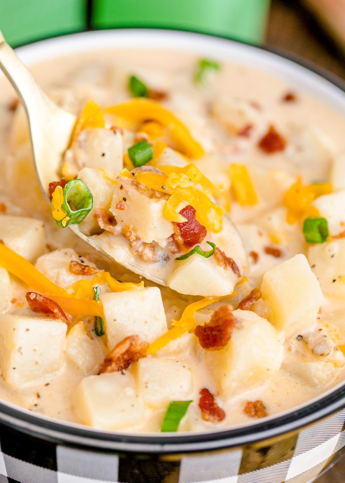 A spoon scooping a bite of slow cooker potato soup out of a bowl.