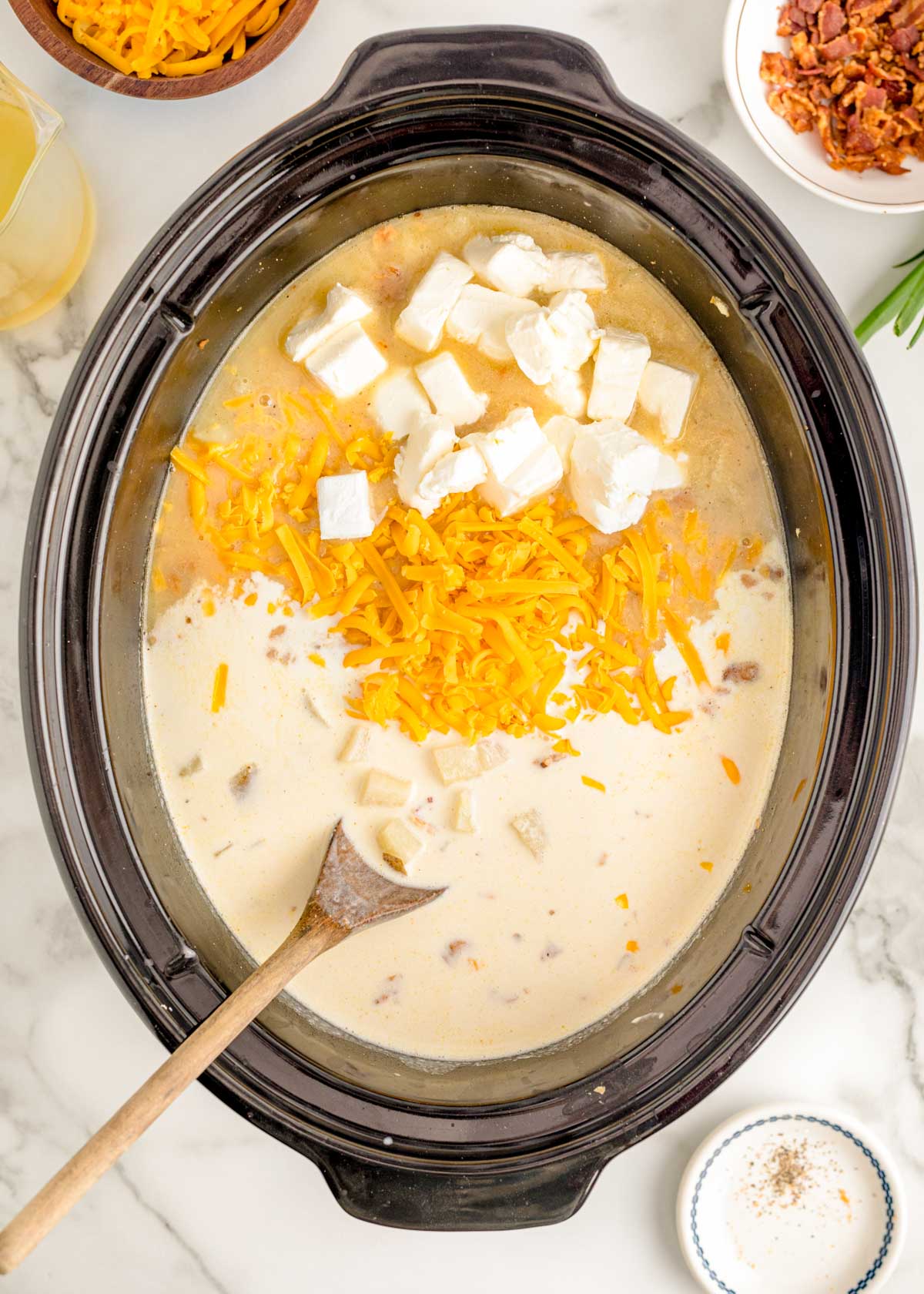 Cheese and heavy cream being added to a crockpot with potato soup.
