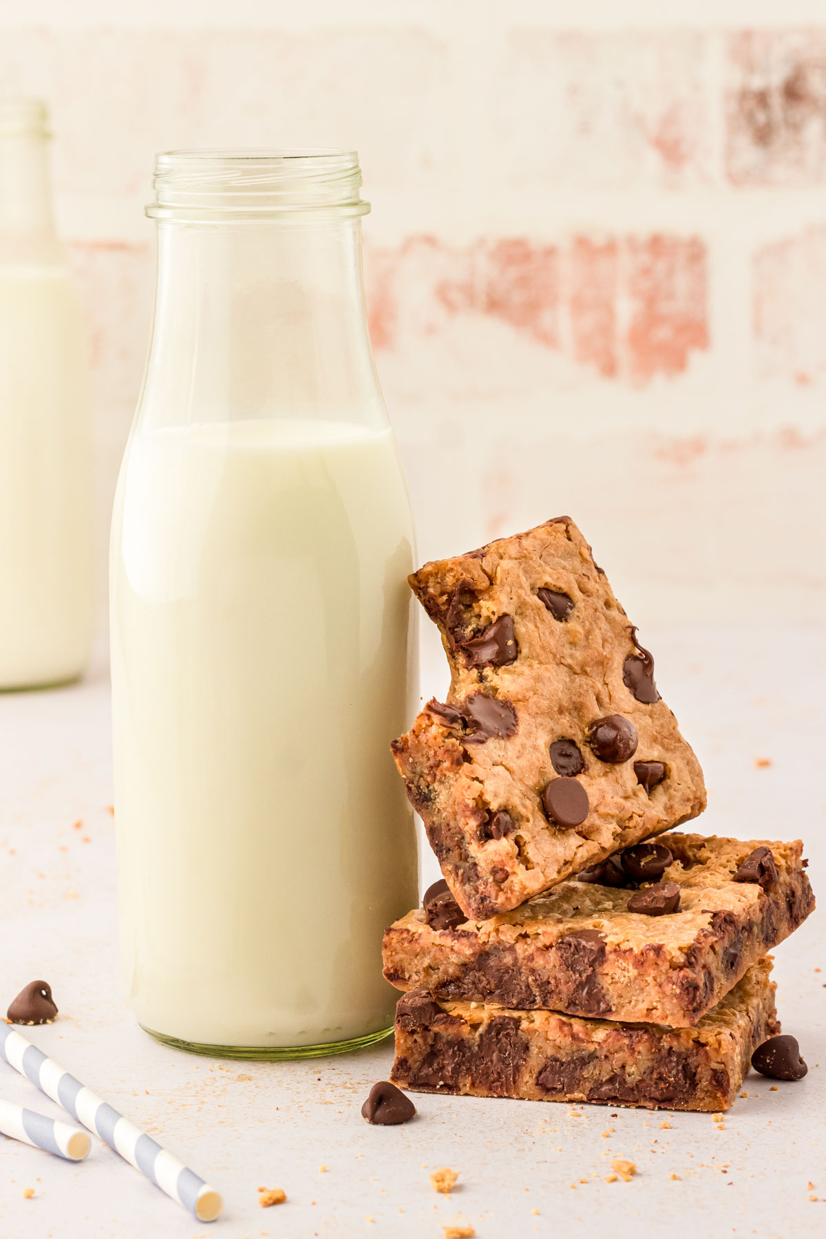 A stack of graham cracker bars next to a milk bottle, the top bar is leaning against it and missing a bite.