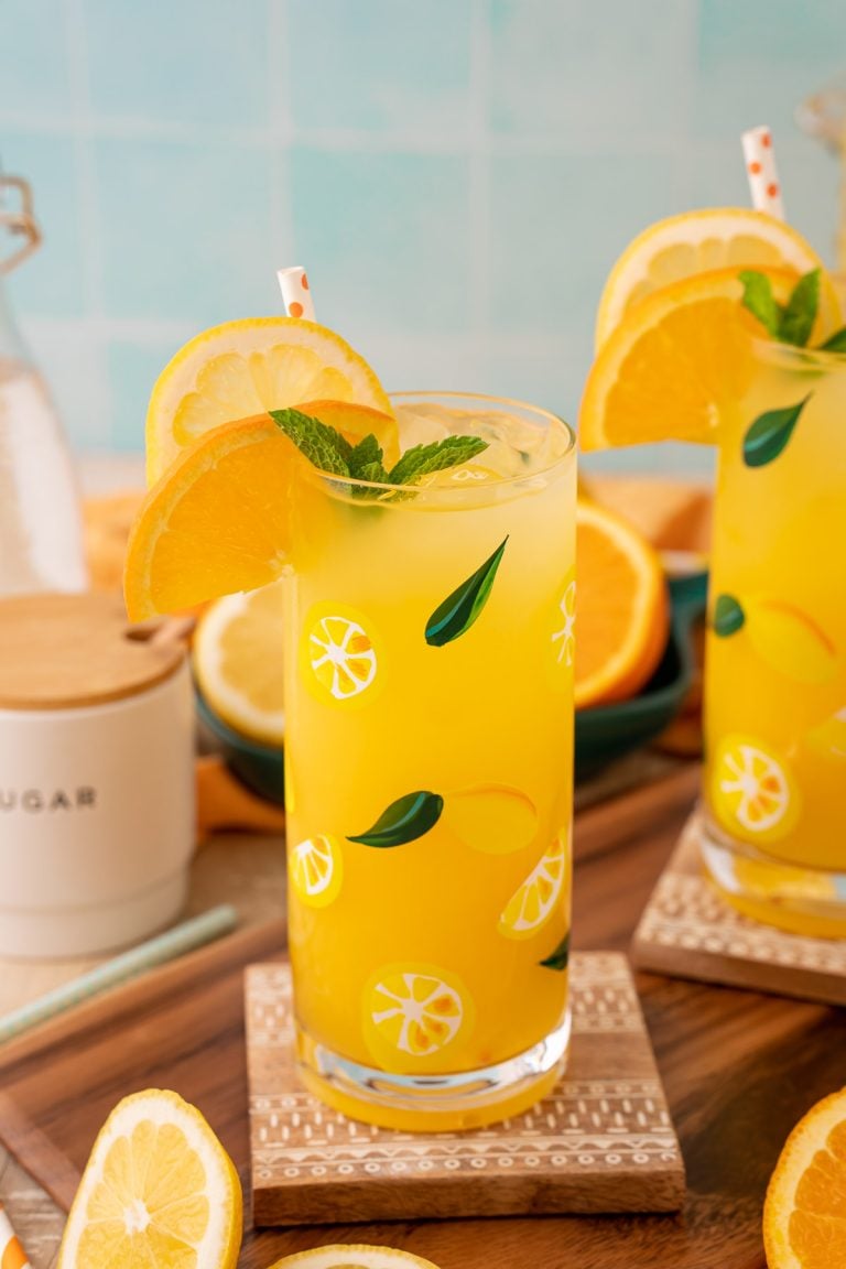 Two glasses of orangeade on coasters with citrus around them.