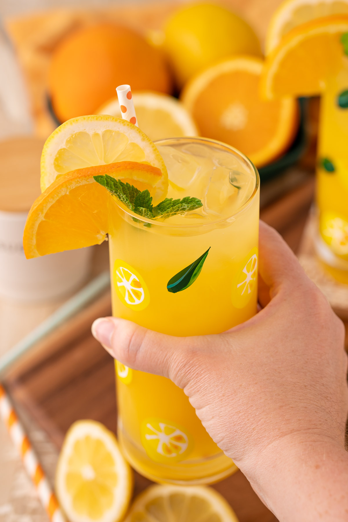 A woman's hand holding a glass of orangeade to the camera.