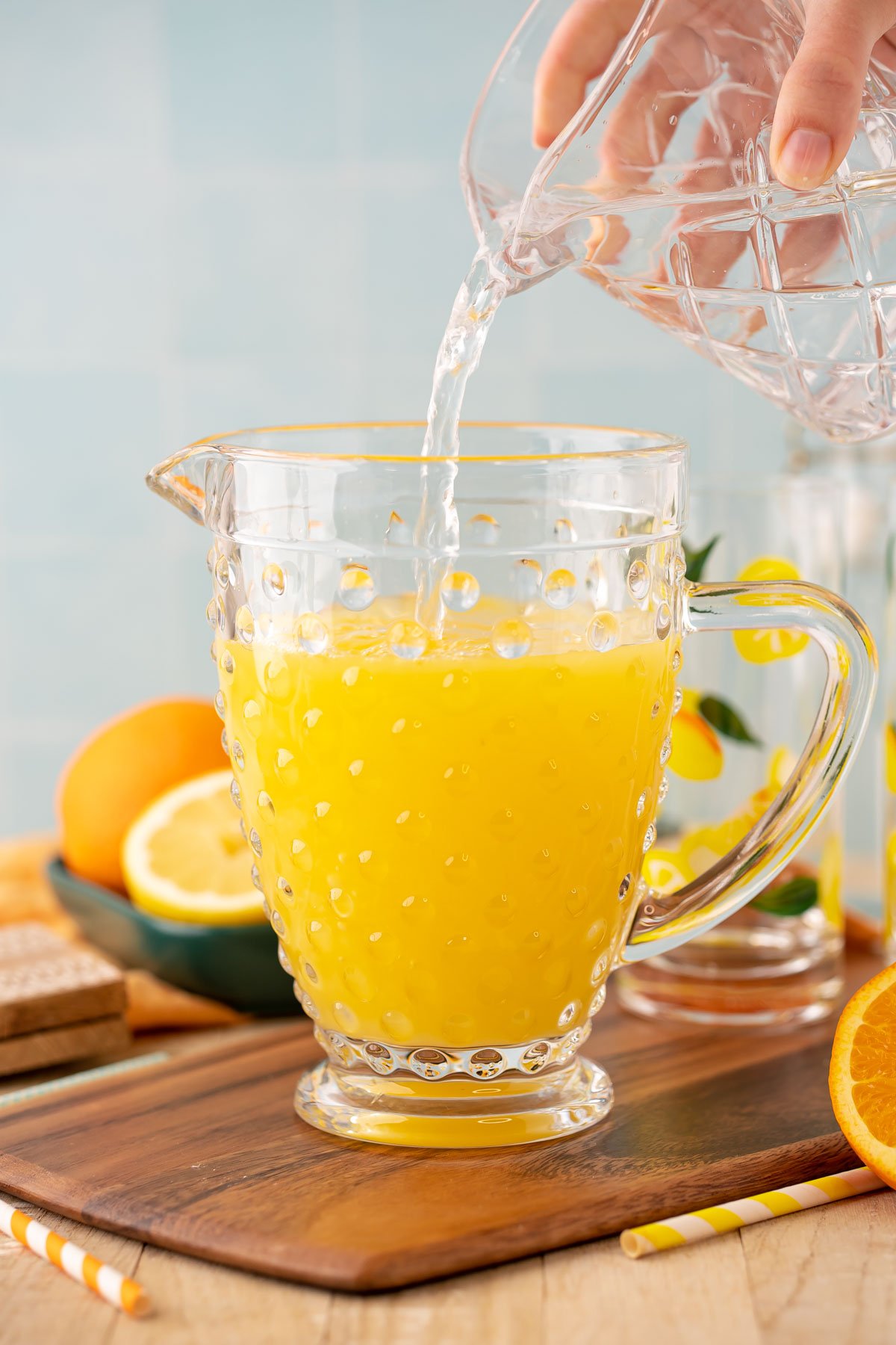 Water being added to a pitcher with orange and lemon juice to make orangeade.