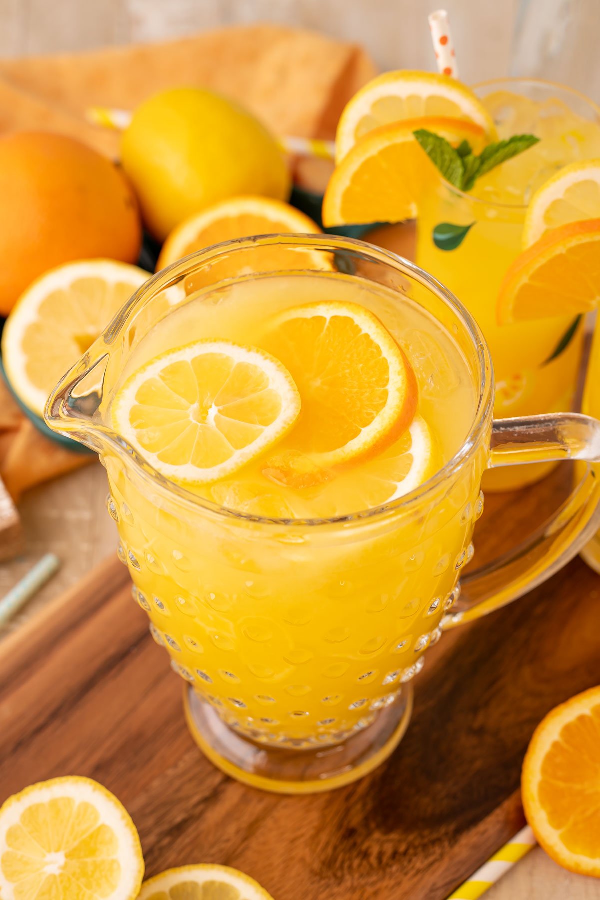 A pitcher of orangeade on a wooden serving board.